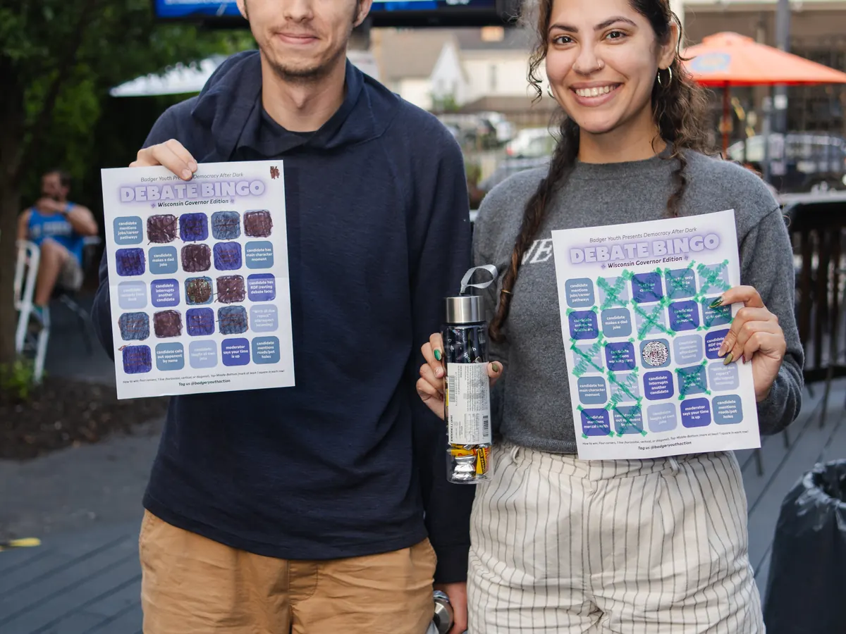 Two participants hold completed bingo cards at a Debate Bingo gathering.