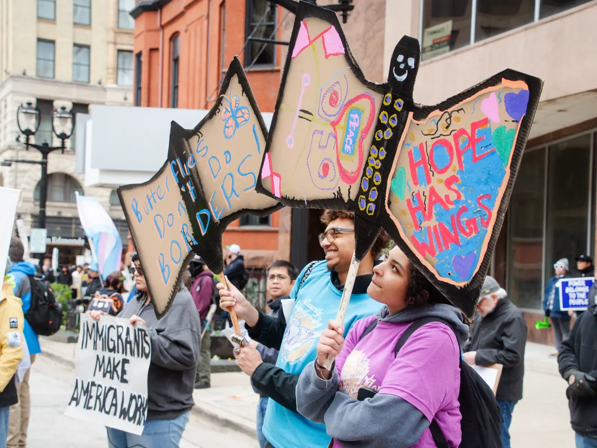 Young people carry handmade butterfly signs at a May Day rally.
