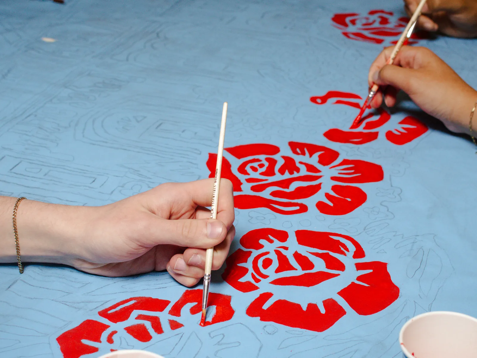 Volunteers paint red flowers across a blue community banner.